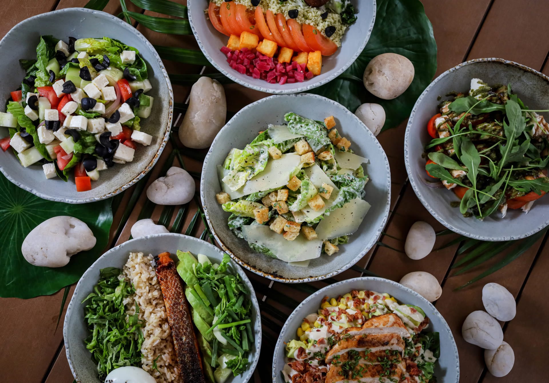 A spread of fresh salads and bowls on a timber table