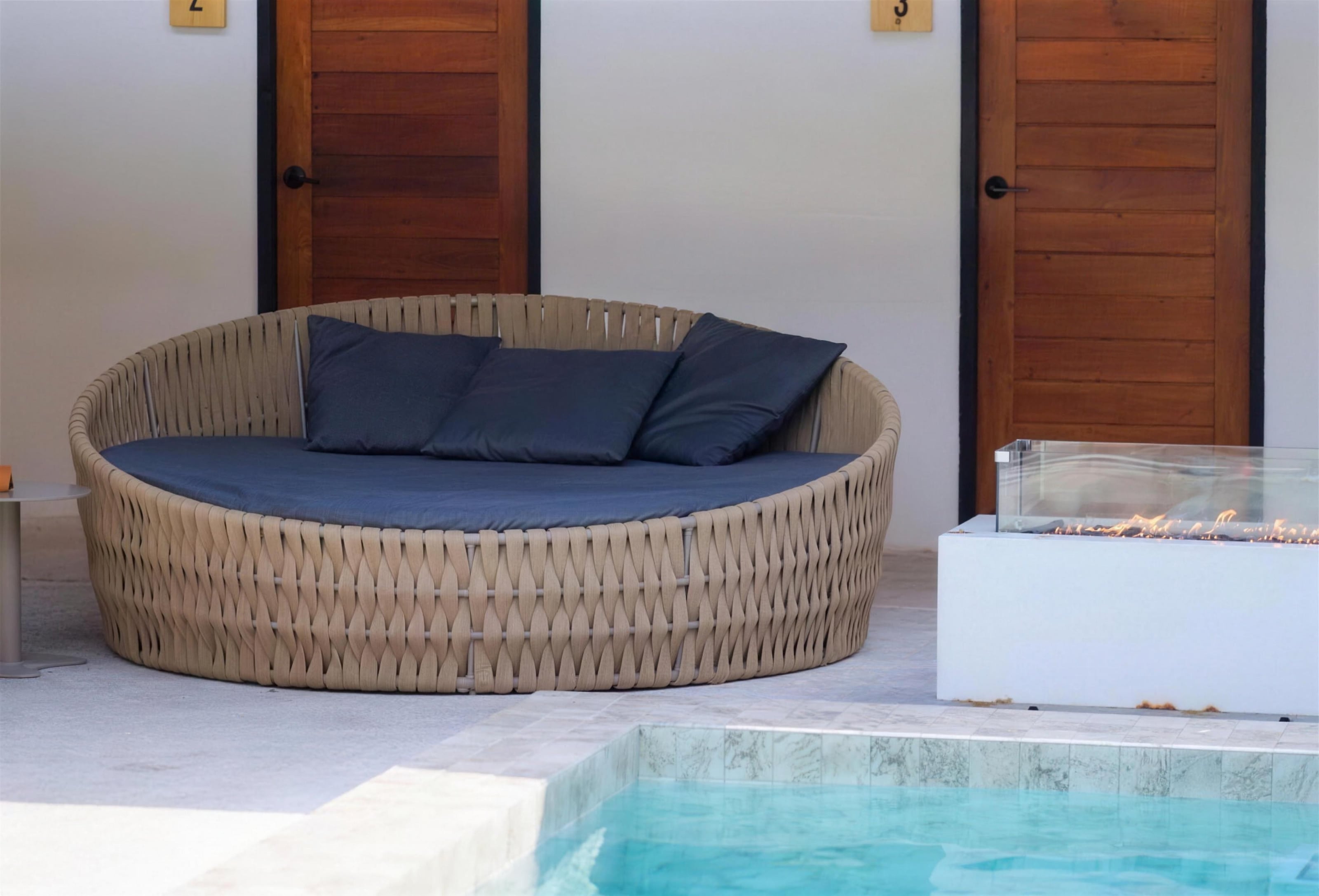 A round rattan daybed beside the plunge pool and fire table