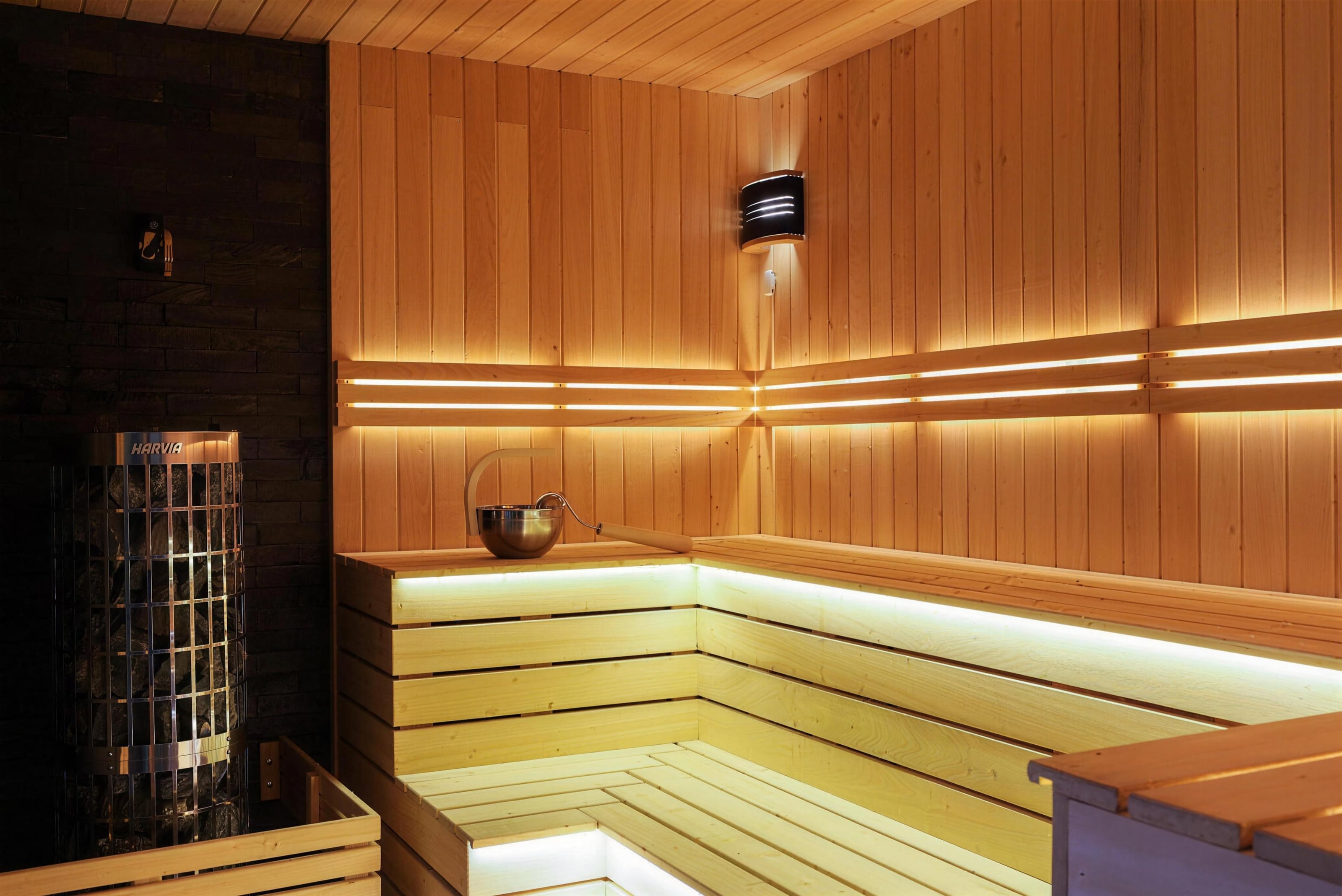 The Finnish sauna: tiered benches glowing under warm light strips beside the stove